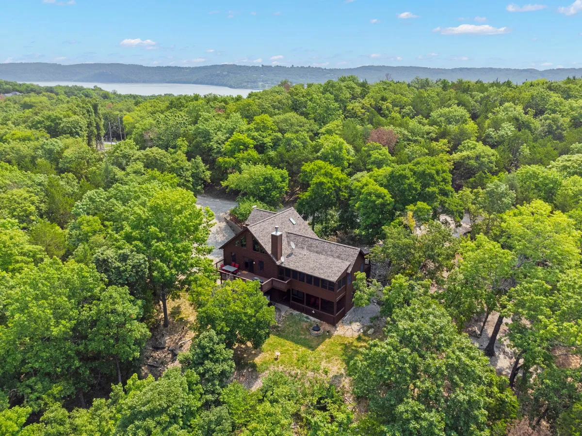 An exterior shot of the house with surrounding trees and a clear view of the lake in the background. The scene radiates tranquility and shows just how close the home is to the water, hinting at easy transitions from lakeside fun back to cabin comfort.