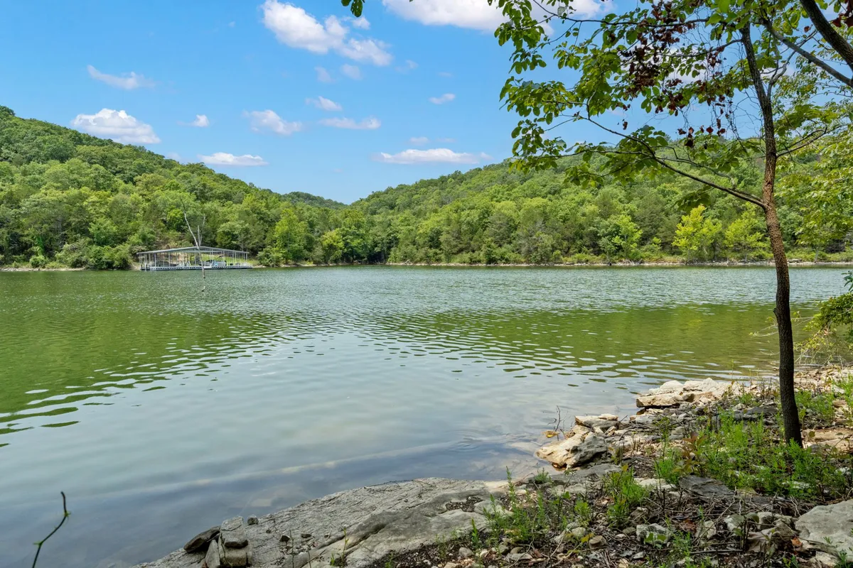 A tranquil view of Table Rock Lake framed by a rocky shoreline, lush green hills, and a calm water surface perfect for swimming, kayaking, and fishing. The natural scenery offers a direct connection to the lake and opportunities for waterfront recreation.