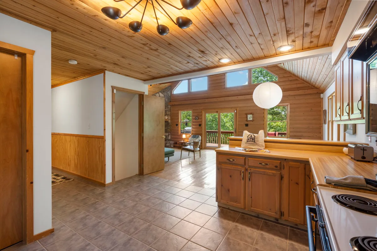 A view of the main living space highlighting wooden ceilings, expansive windows, a central kitchen island, and a comfortable seating area. The natural light and inviting decor suggest a seamless flow between cooking, entertaining, and relaxing.
