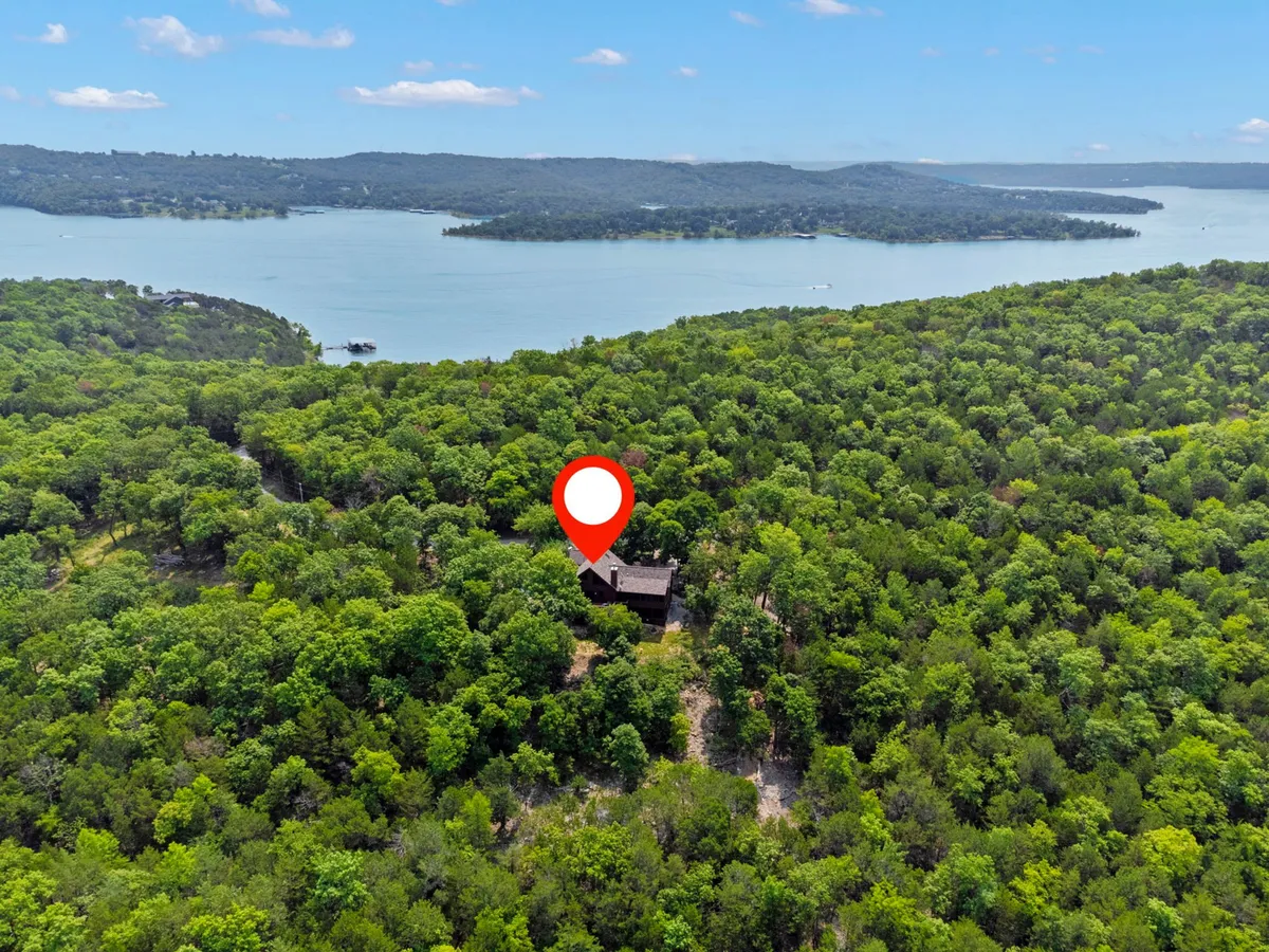 This exterior image shows the Buffalo Bluff house nestled amidst tall trees, with the tranquil lake just beyond and the soft glow of sunset in the background. The scene exudes peace and seclusion, emphasizing the property's proximity to the water and its natural surroundings.