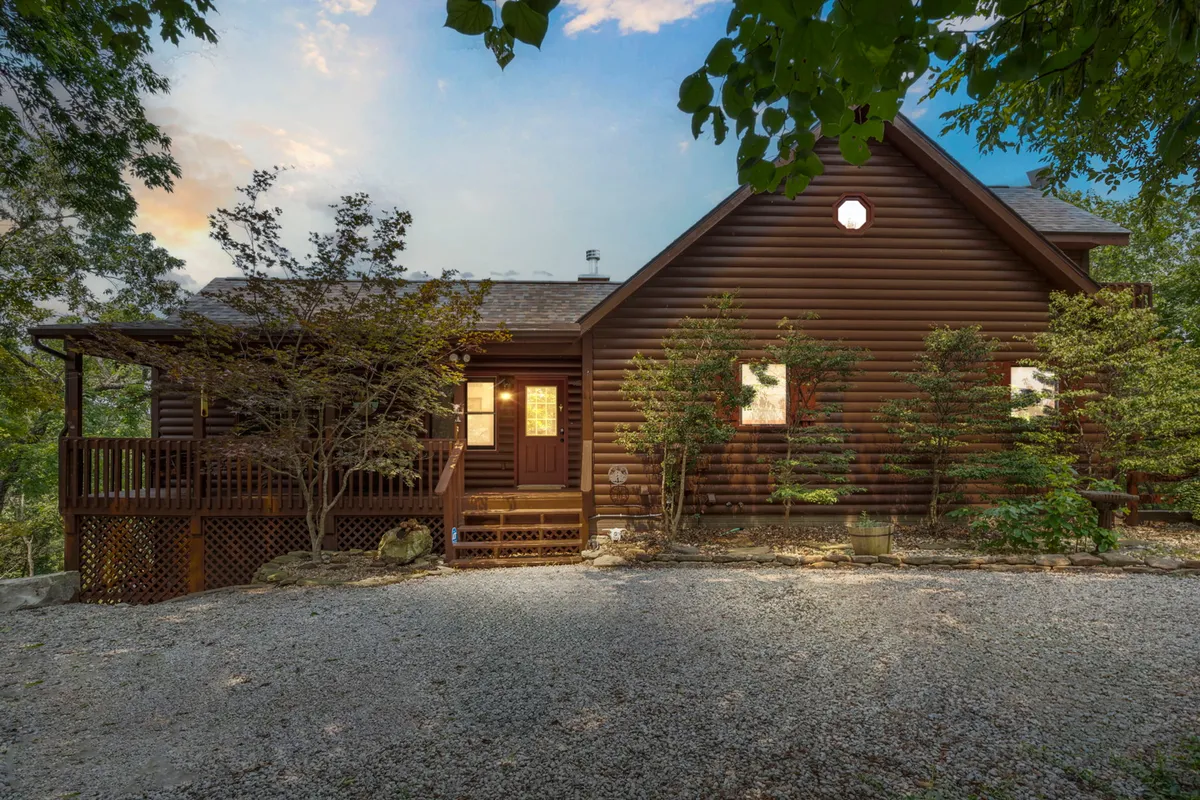 A warm exterior perspective of the log cabin structure with its wooden deck surrounded by a landscaped garden. The space invites outdoor relaxation and family gatherings, with a backdrop of trees ready for sunset or sunrise moments.