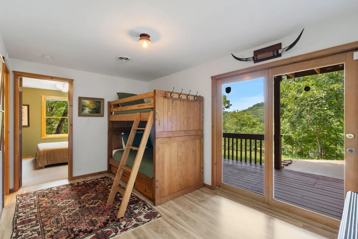 A comfortable bunk bed is the centerpiece, set near large glass doors that open to beautiful nature views. The space feels welcoming, with a soft rug and plenty of natural light streaming in.